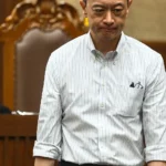 Tom Lembong dalam ruang sidang dilihat dari sudut atas, mengenakan kemeja putih bergaris dan ekspresi serius di tengah proses hukum.