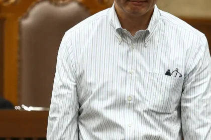 Tom Lembong dalam ruang sidang dilihat dari sudut atas, mengenakan kemeja putih bergaris dan ekspresi serius di tengah proses hukum.