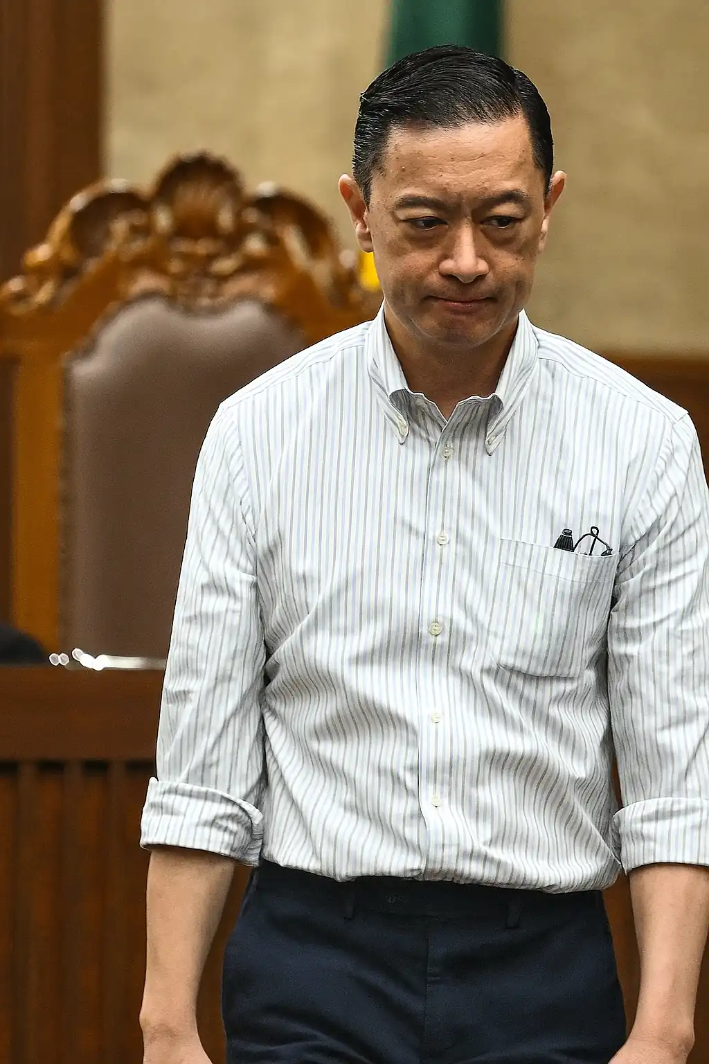 Tom Lembong dalam ruang sidang dilihat dari sudut atas, mengenakan kemeja putih bergaris dan ekspresi serius di tengah proses hukum.